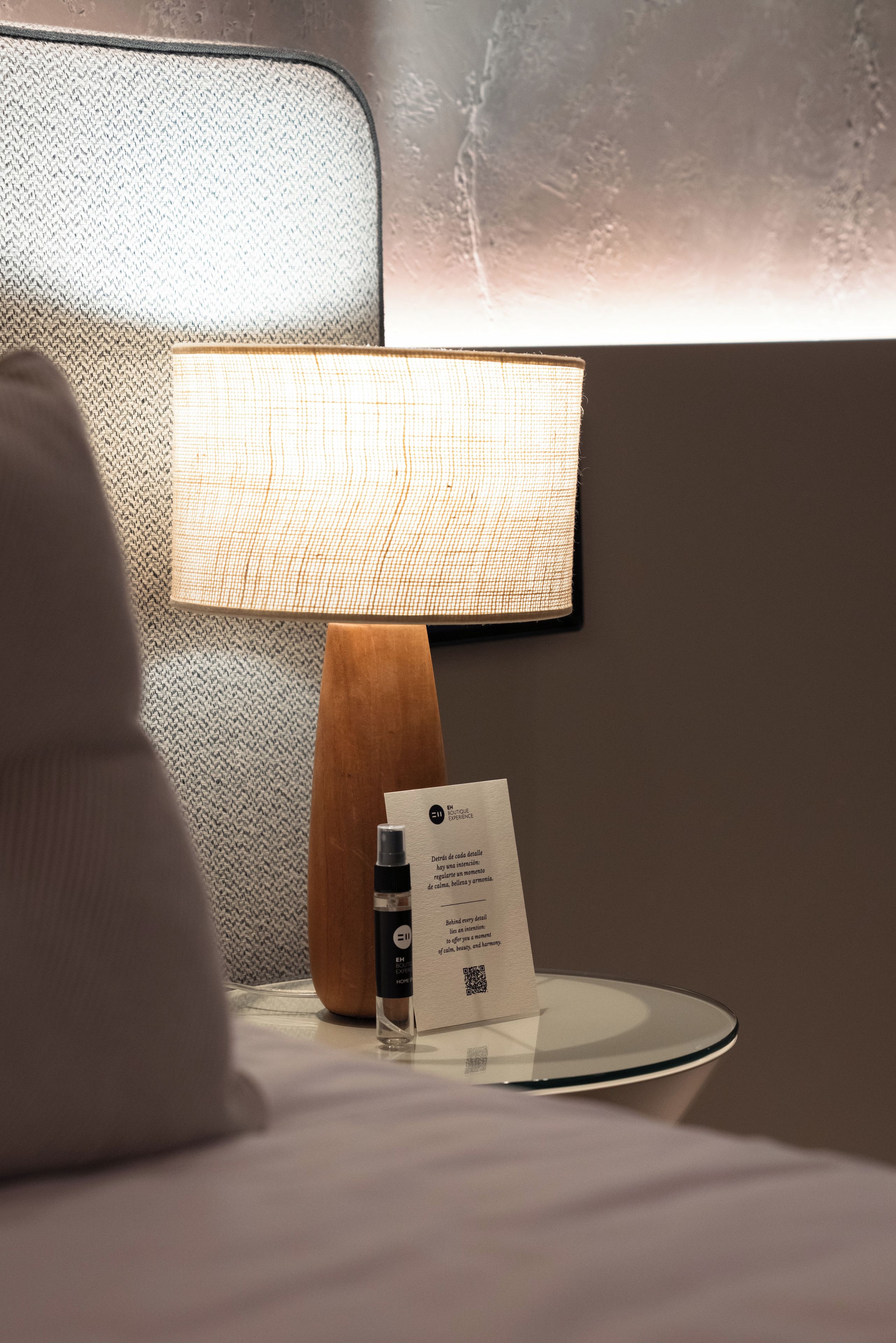 A bedside table with a lamp, a bottle, and a card.