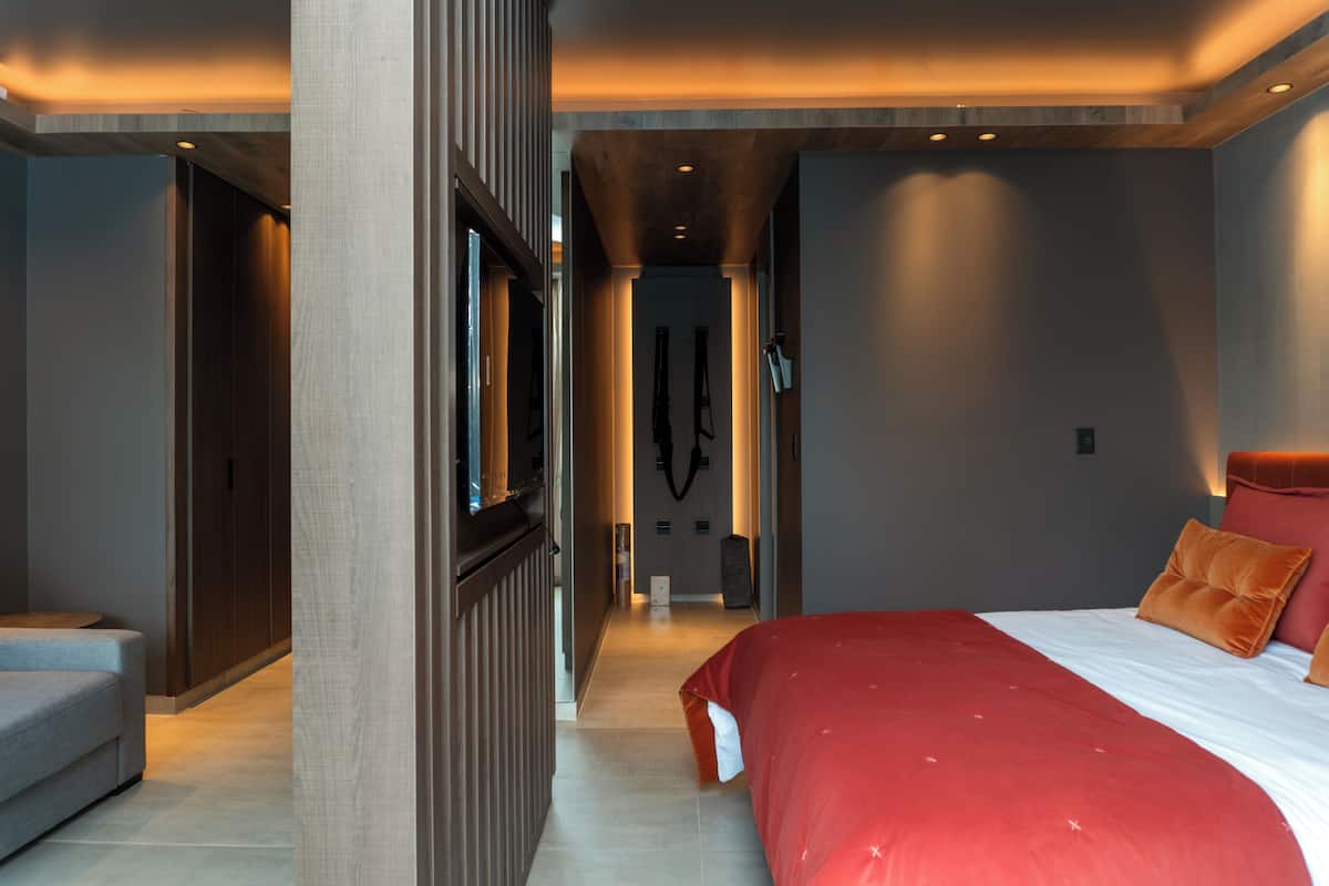 A modern hotel room with a large bed, a seating area, and a hallway leading to a bathroom.