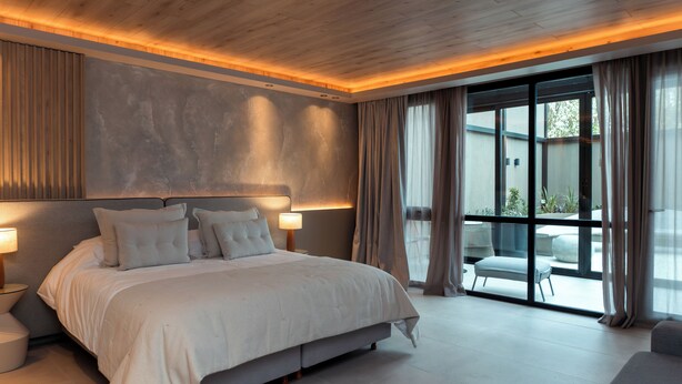 Une chambre à coucher moderne, dotée d’un grand lit, de lampes de chevet et offrant une vue sur l’extérieur grâce à de grandes fenêtres.