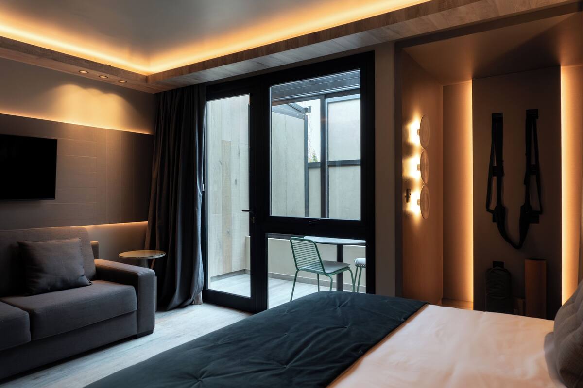 A modern hotel room with a bed, a sofa, a small table, and a balcony with a chair.