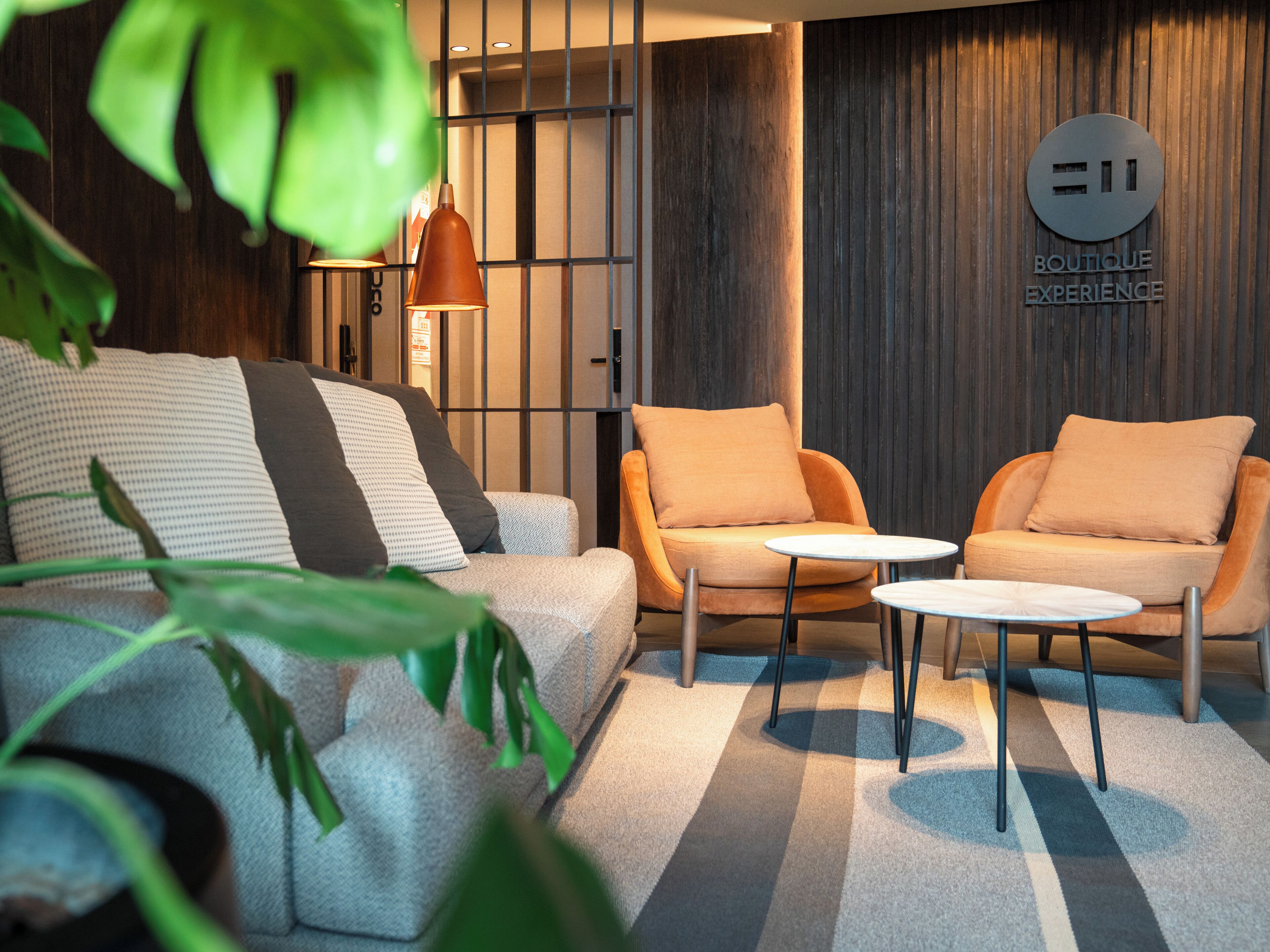 A modern lounge area with a sofa, two armchairs, and a small table. A sign on the wall reads "BOUTIQUE EXPERIENCE."