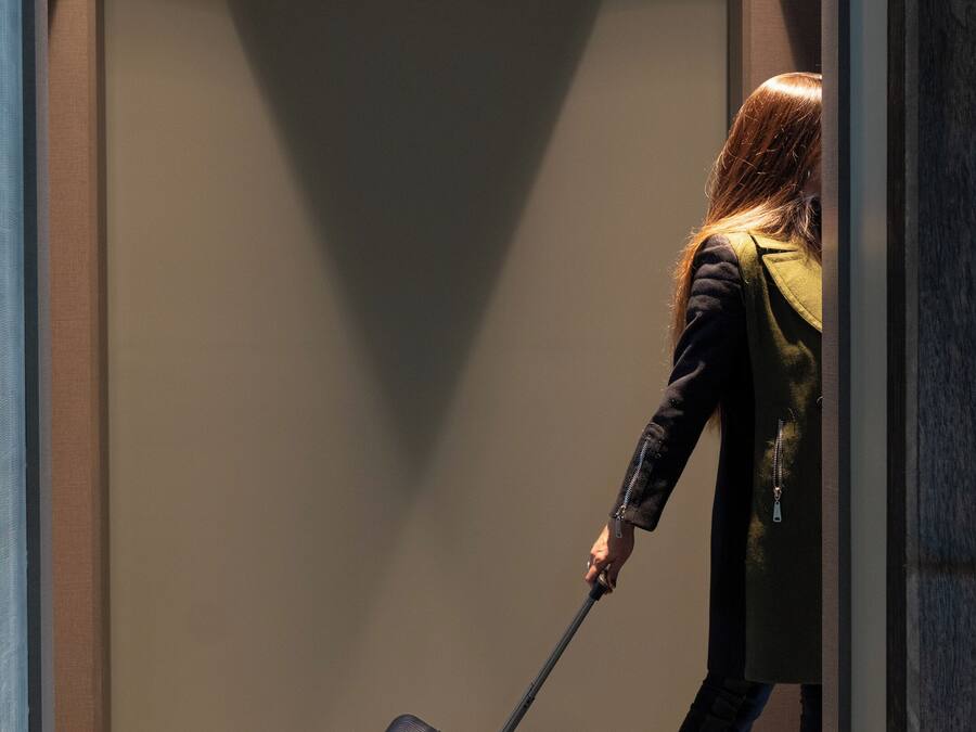 A person pulling a suitcase through a narrow hallway with a ceiling that has a grid pattern.