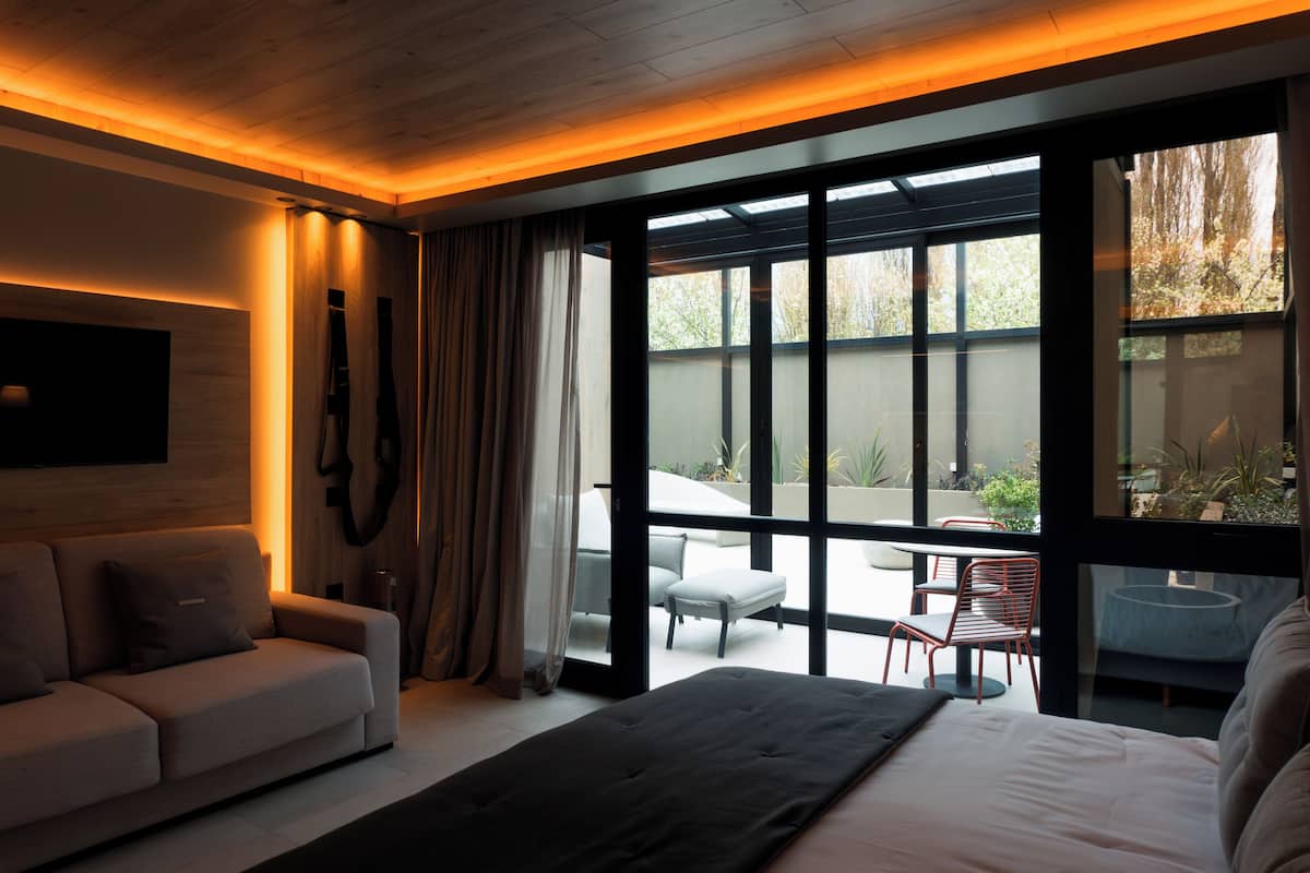 A modern bedroom with a large bed, a sofa, and a view of an outdoor patio with seating.