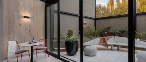 A modern outdoor seating area with a glass partition, a round table, and chairs.