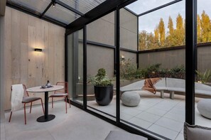A modern outdoor seating area with a glass partition, a round table, and chairs. - Eh Boutique Experience (El Calafate)