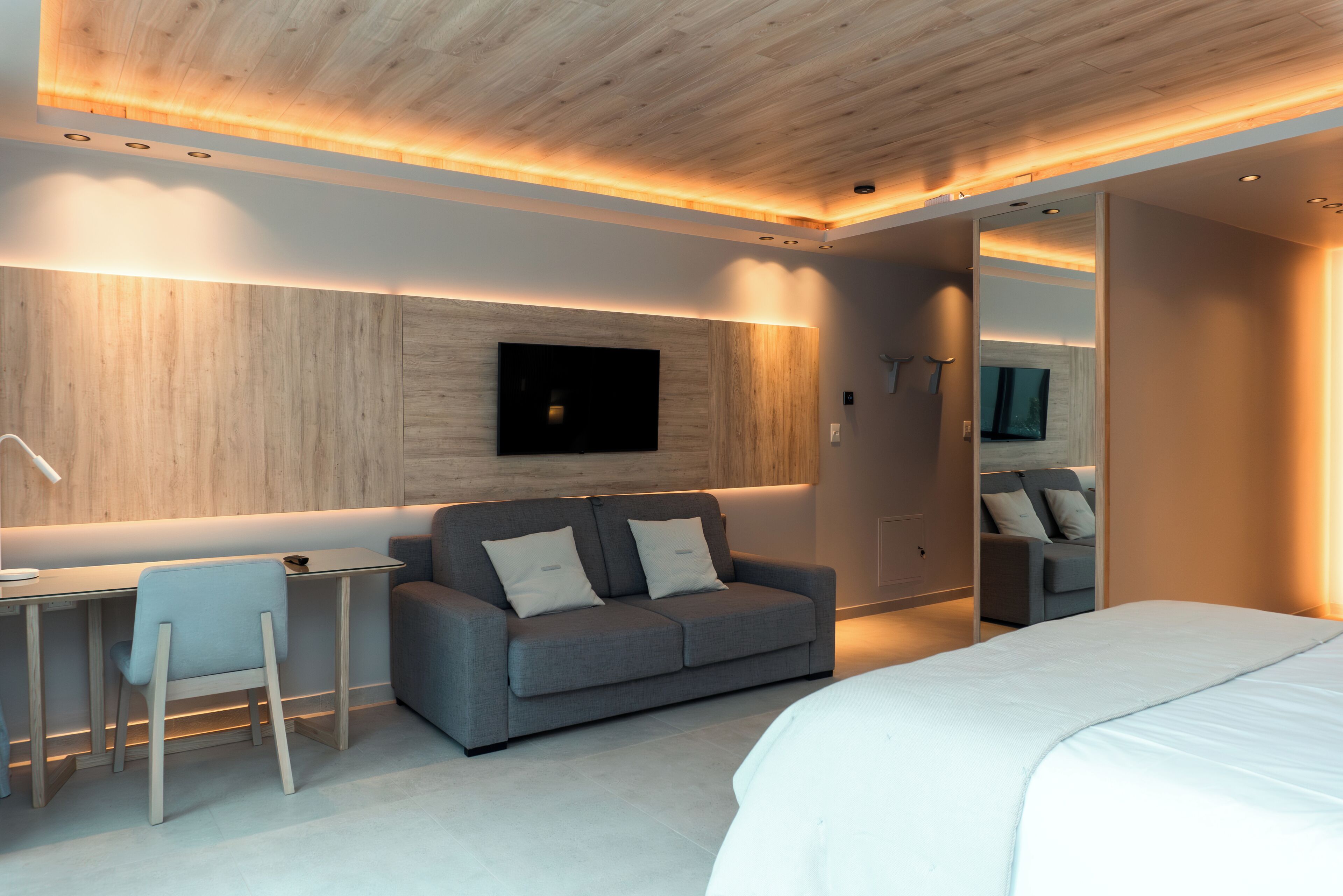 A modern bedroom with a bed, a gray sofa, a desk, and a mirror.
