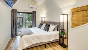 Une chambre avec un grand lit, un téléviseur fixé au mur et une fenêtre avec des rideaux.
