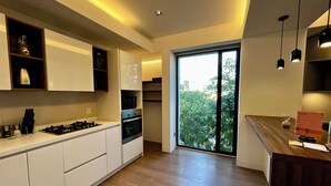 A modern kitchen with white cabinets, a wooden countertop, and a large window with a view of trees.