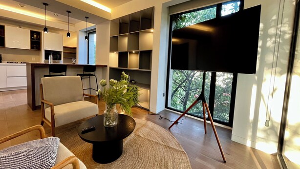 A modern living room with a round coffee table, a sofa, a TV on a stand, and a large window with a view of trees.