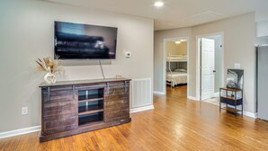 A modern living room with a flat-screen TV mounted on the wall, a wooden entertainment unit, and a hallway leading to a bedroom with bunk beds. - Home 14 Mi to Highpoint Health w/ Fenced Yard! (Hendersonville)