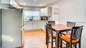 A modern kitchen with white cabinets, a stainless steel refrigerator, wooden dining table, and chairs. - Home 14 Mi to Highpoint Health w/ Fenced Yard! (Hendersonville)