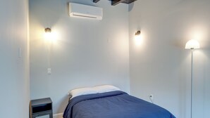 A bedroom with a bed, bedside tables, an air conditioner, and wall-mounted lights.