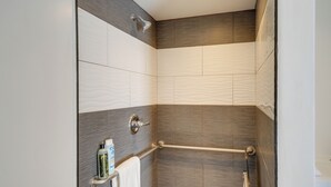 Et bruseområde med gelænder, et håndklædestativ med toiletartikler og en væg med struktur.