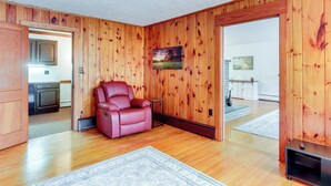 A spacious living room with wooden walls, a red leather sofa, a small table, and a rug. - Biglerville Getaway w/ Creek & Fireplace! (Biglerville)