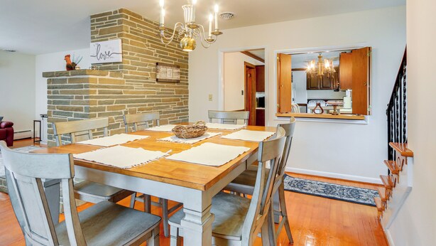 A dining area with a wooden table, white placemats, and a stone accent wall. - Biglerville Getaway w/ Creek & Fireplace! (Biglerville)