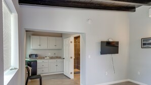 A modern kitchen with white cabinets, a microwave, and a sink. There is a door leading to a bathroom with a shower. A flat-screen TV is mounted on the wall. - 6 Mi to Frazier Mountain: Cozy Studio Retreat (Frazier Park)