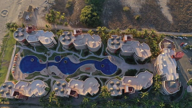 An aerial view of a resort with multiple buildings, a central swimming pool, and surrounding palm trees. - 3 bedrooms, fabulous pools on 15 km of quiet, beautiful Pacific Coast beach (LaCulebra)