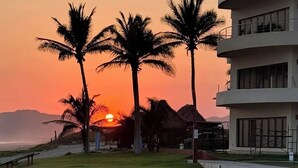 A modern building with a curved facade, palm trees, and a sunset in the background. - 3 bedrooms, fabulous pools on 15 km of quiet, beautiful Pacific Coast beach (LaCulebra)