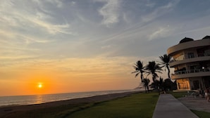 A beachfront hotel with a sunset view, a grassy area, and palm trees. - 3 bedrooms, fabulous pools on 15 km of quiet, beautiful Pacific Coast beach (LaCulebra)