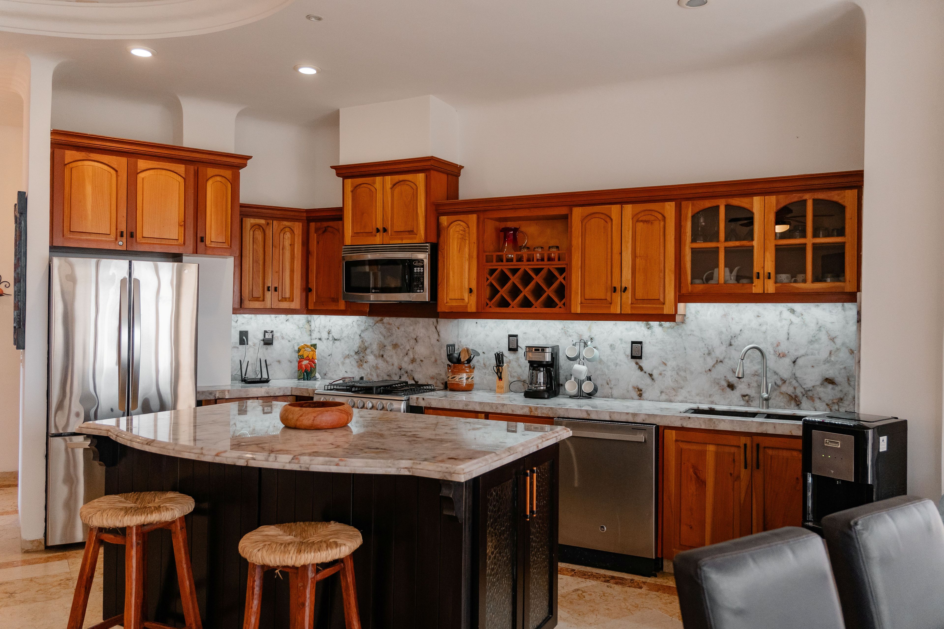 A kitchen with wooden cabinets, a stainless steel refrigerator, a microwave, and a marble countertop.