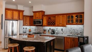 A kitchen with wooden cabinets, a stainless steel refrigerator, a microwave, and a marble countertop.