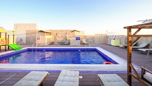 A rectangular pool with a blue tiled edge, surrounded by lounge chairs and a wooden deck. - Abraj INN Royal Hotel (Doha)