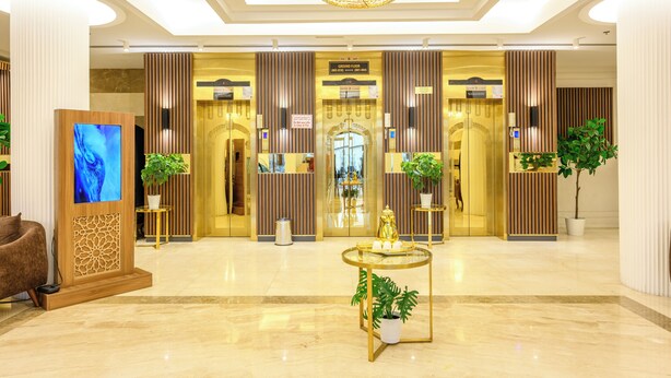 A modern lobby with a marble floor, a reception desk, a television screen, and potted plants. - Abraj INN Royal Hotel (Doha)