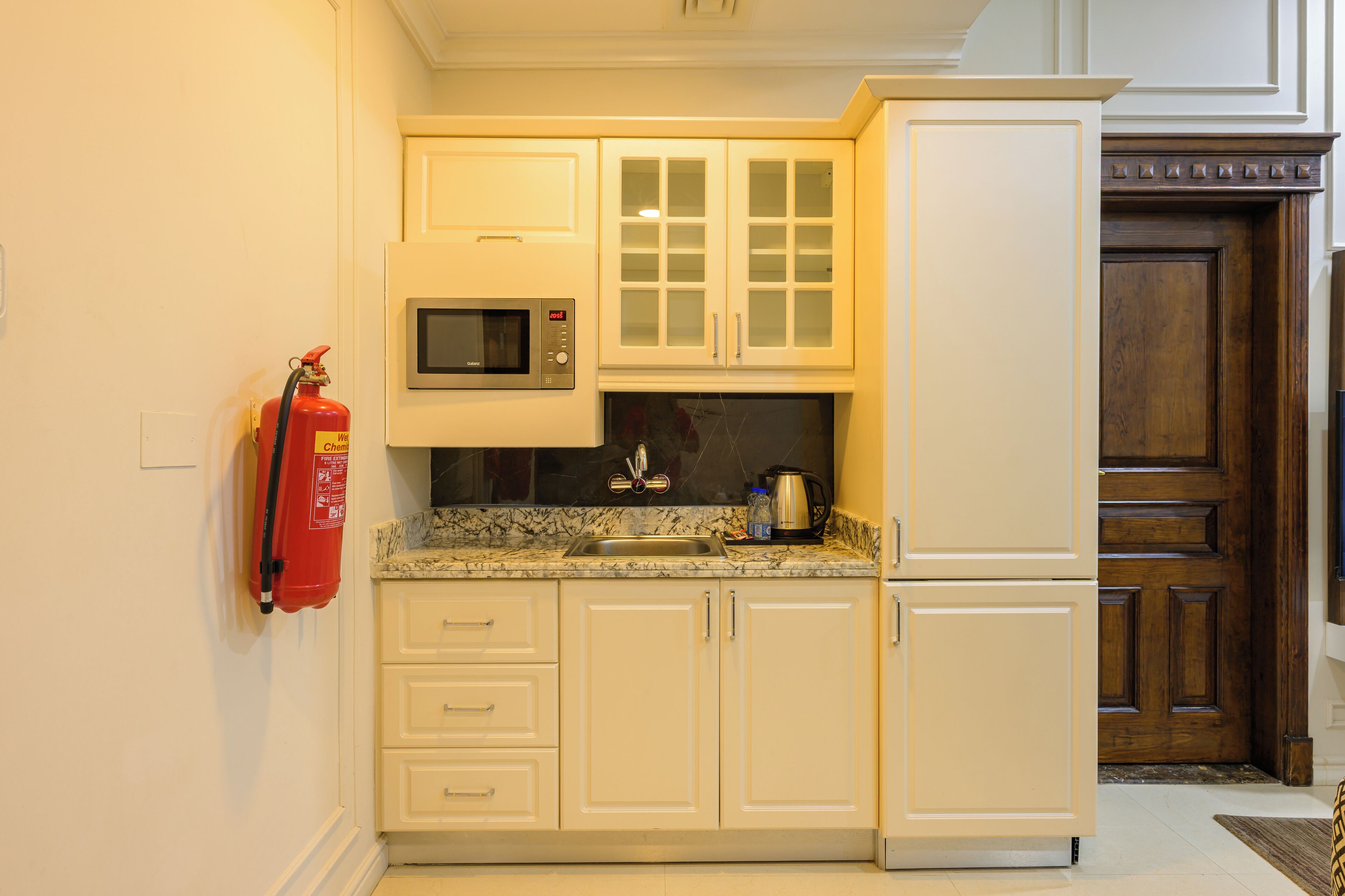 A kitchen with white cabinets, a microwave, a coffee maker, and a fire extinguisher.