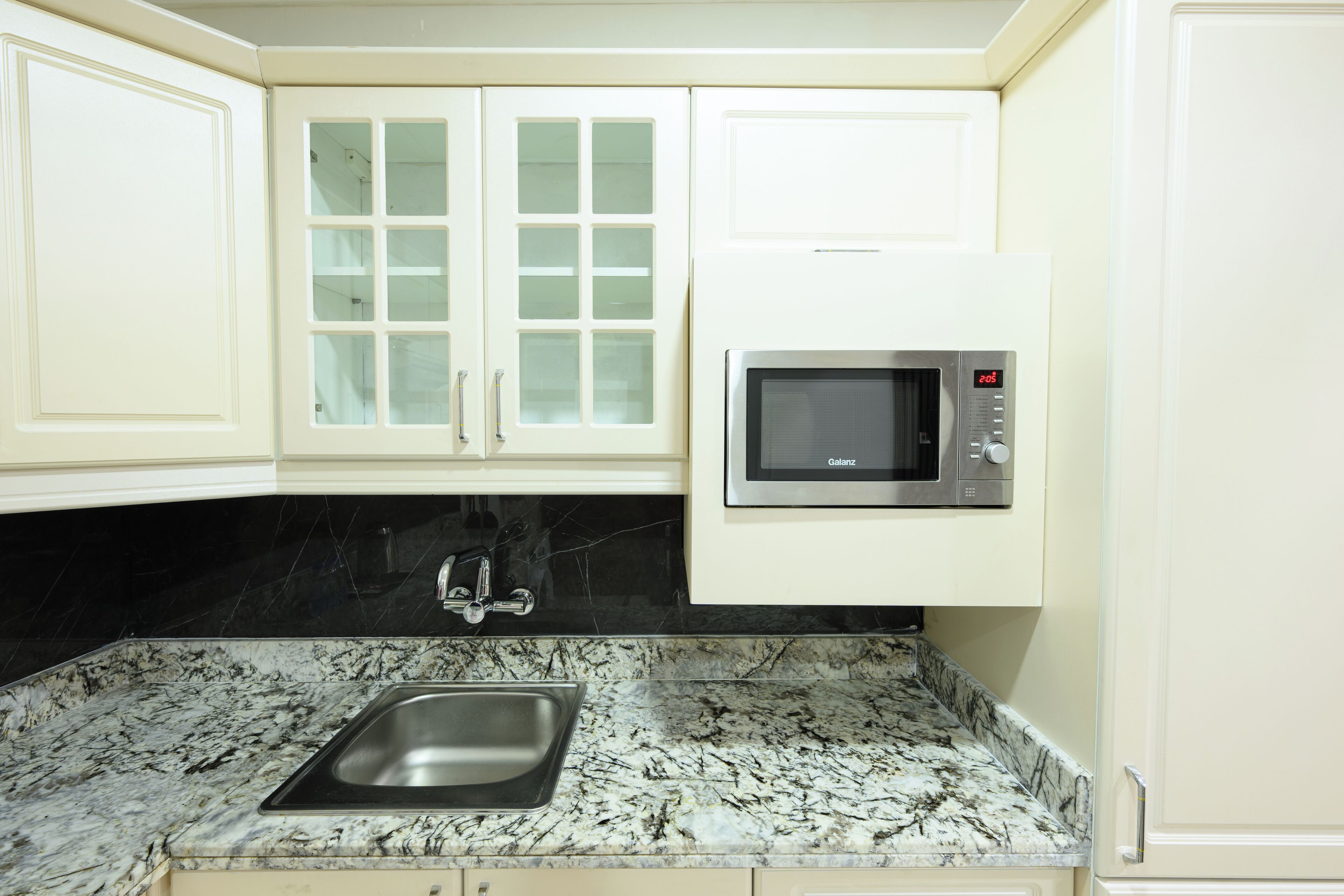 A kitchen with white cabinets, a black countertop, and a stainless steel sink.