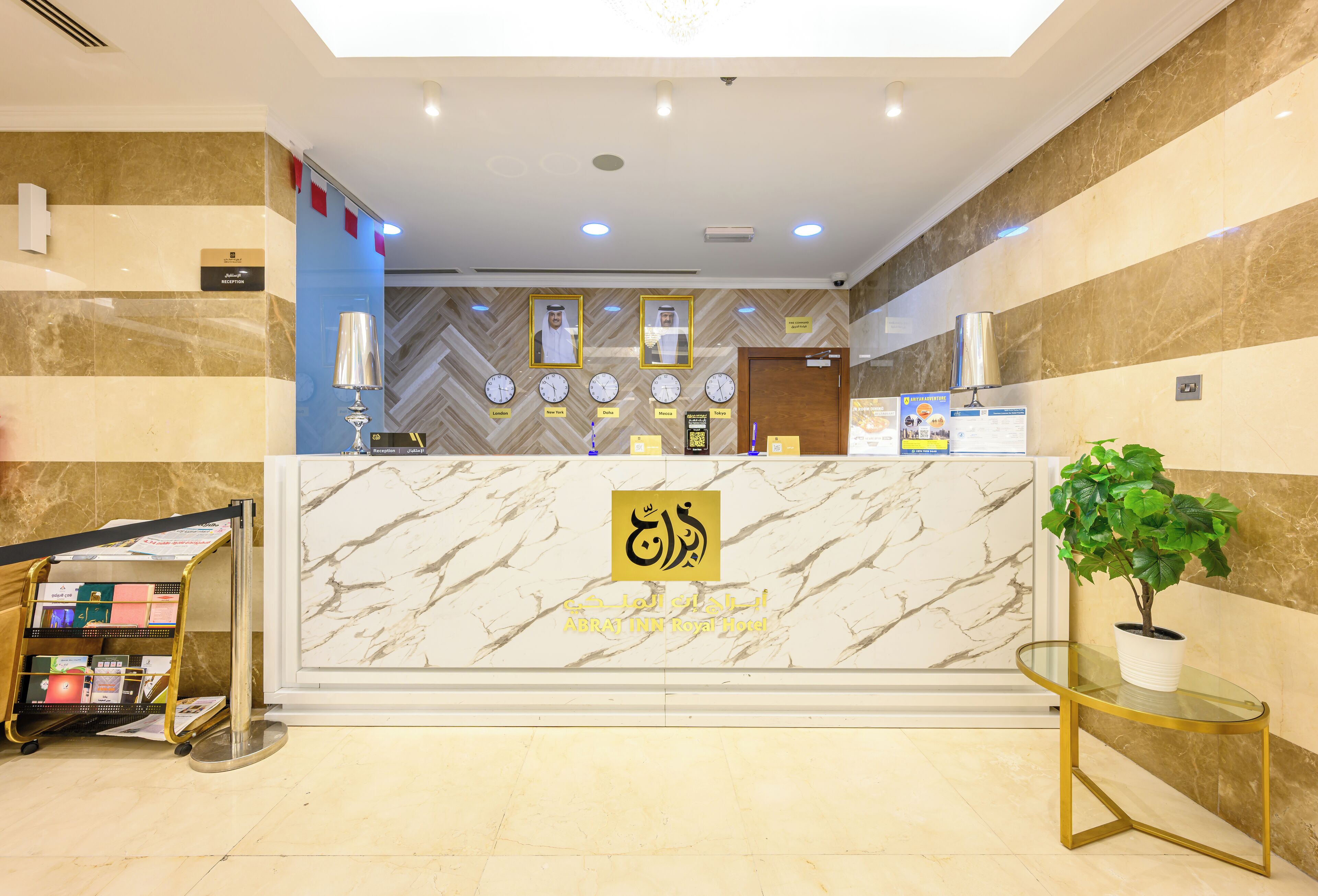 Zona de recepción de un hotel con un mostrador de mármol, una barra de recepción, un reloj con múltiples zonas horarias y un cartel de recepción.