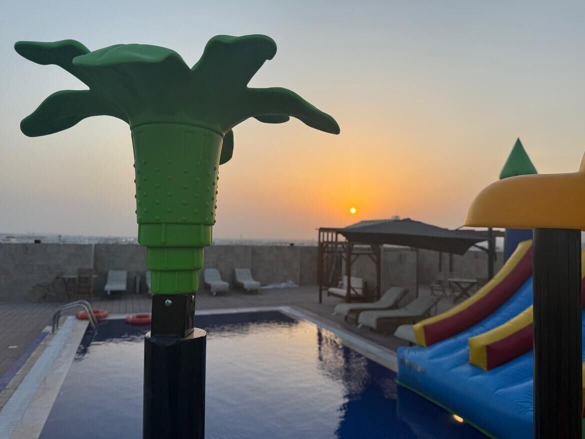 Zona de piscina con tobogán, sillas de descanso y un atardecer de fondo.