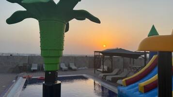 Zona de piscina con tobogán, sillas de descanso y un atardecer de fondo.