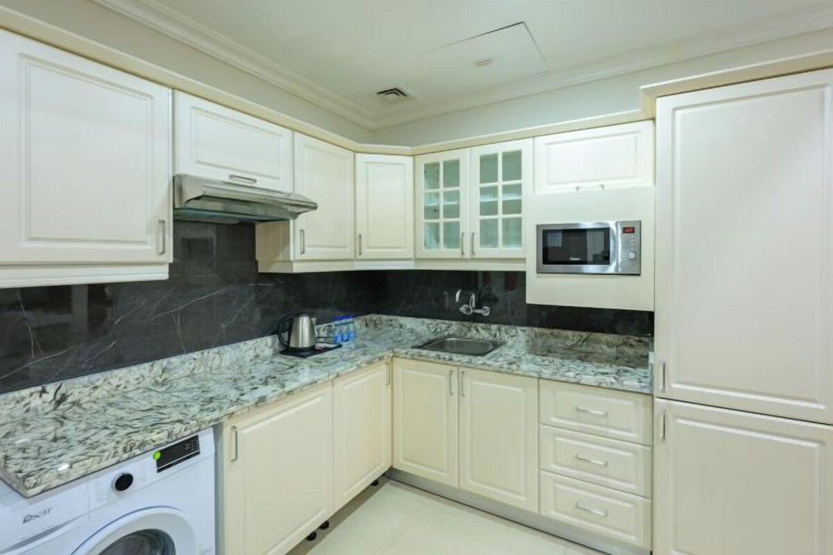 A kitchen with white cabinets, a black marble countertop, a microwave, and a washing machine.