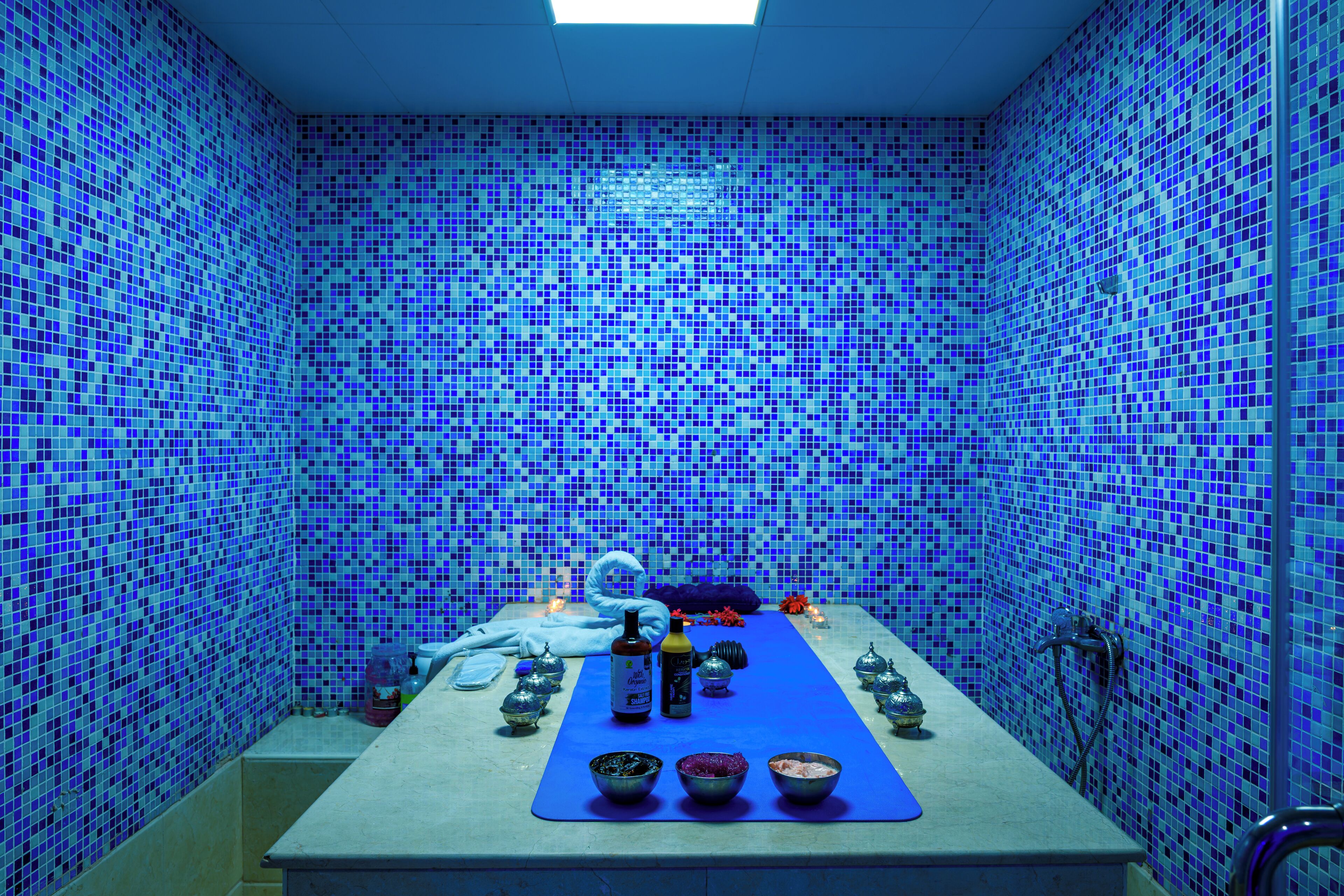 A room with a blue mosaic tiled wall, a long table with various items, and a ceiling light.