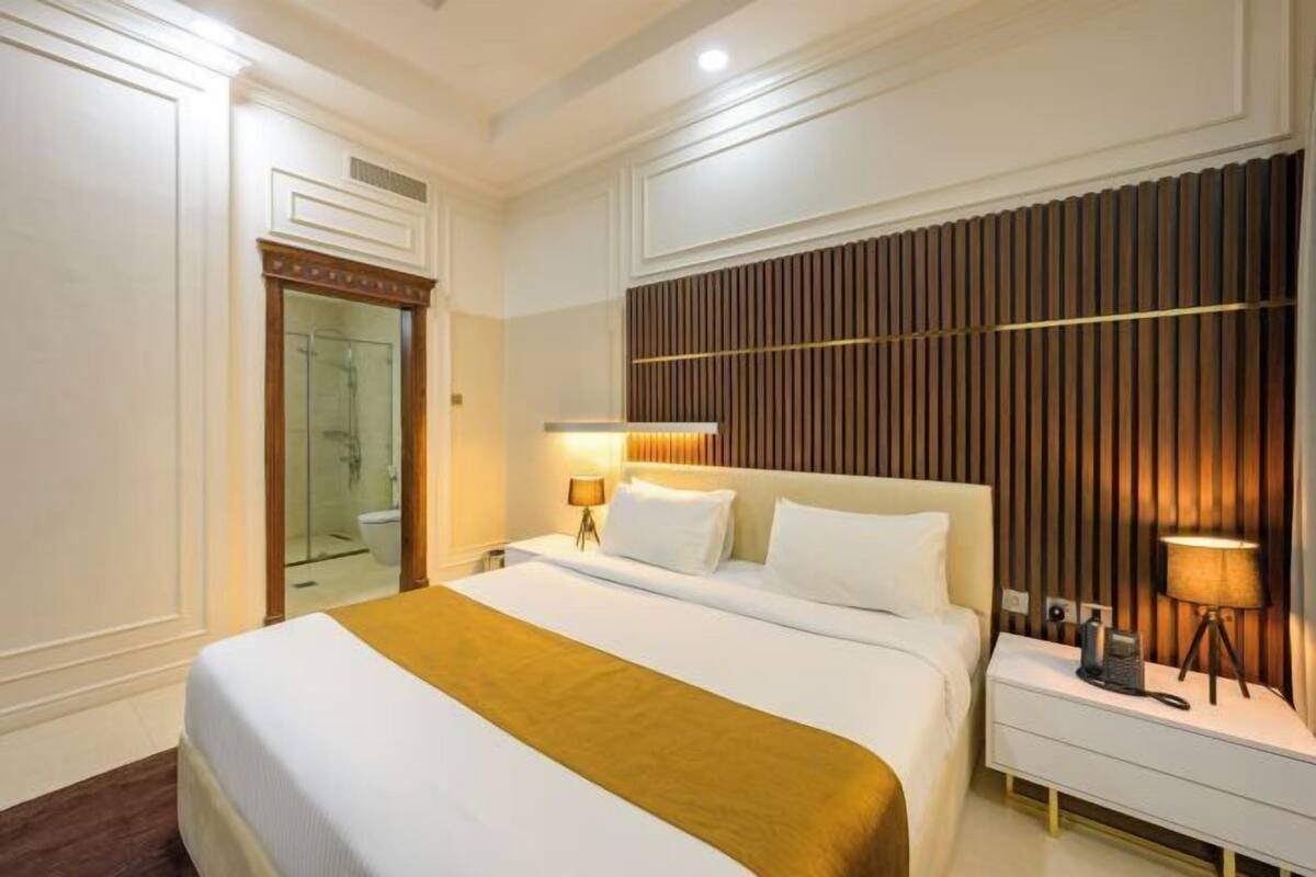 A hotel room with a large bed, bedside tables, a mirror, and a wooden panel wall.