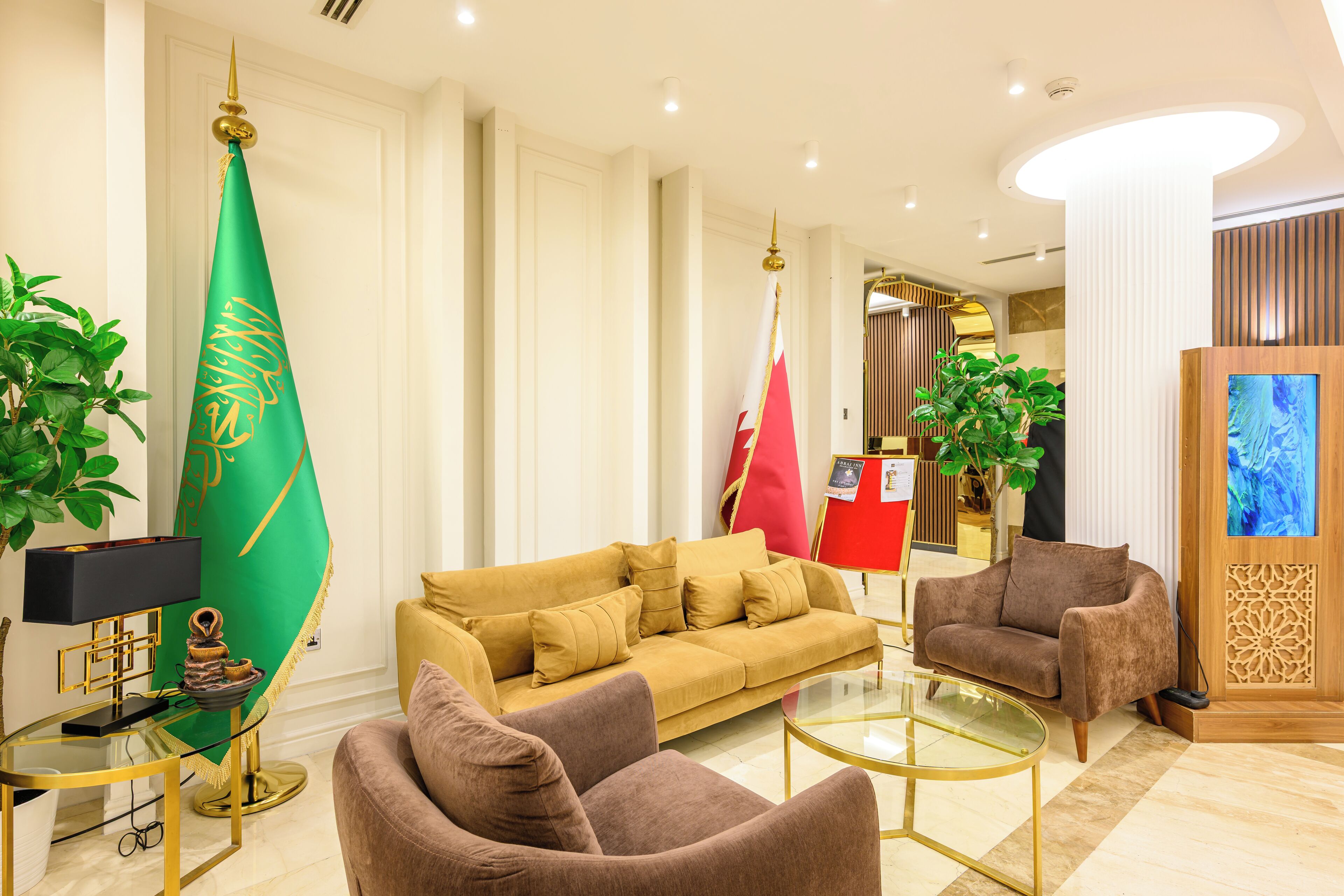 A modern hotel lobby with a sofa, armchairs, a TV, and flags.