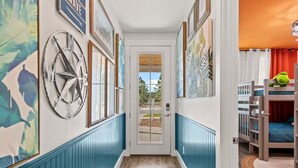 A hallway with a door leading to a room with bunk beds, framed artwork on the walls, and a window with blinds.