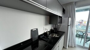 A modern kitchen with a black countertop, stainless steel appliances, and a large window with a city view. - RN STUDIO - APTO 620 (Maceio)