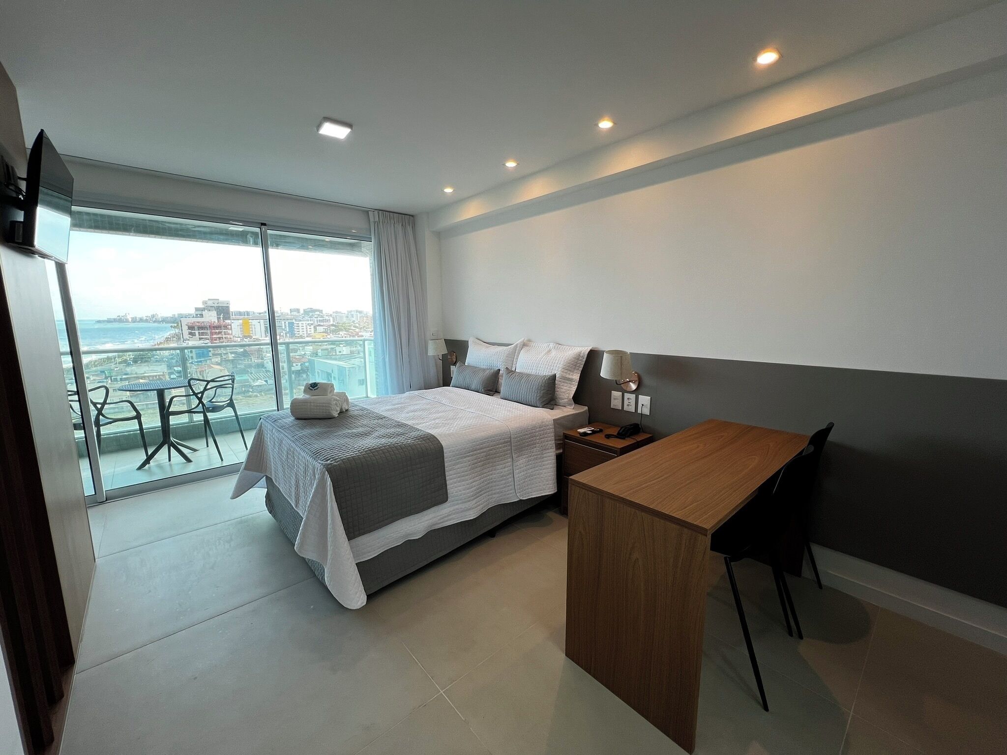 Una habitación de hotel moderna con una cama grande, un escritorio de madera y un balcón con vista a la ciudad.