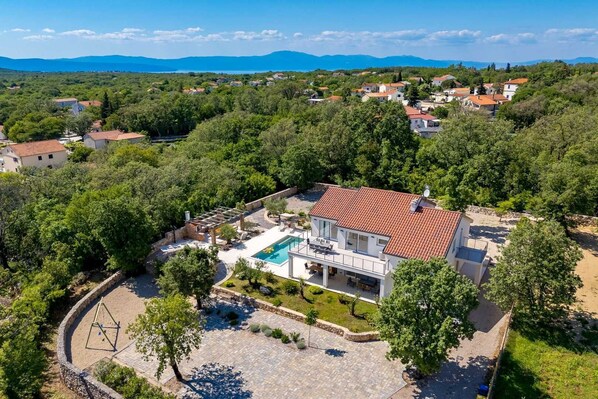 Una casa moderna con piscina, rodeada de abundante vegetación y un paisaje montañoso.