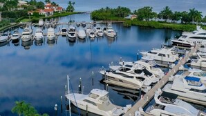 A marina with multiple boats docked, surrounded by greenery and a distant building.