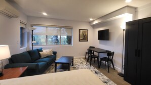 Une chambre d’hôtel compacte comprenant un canapé, une petite table, un bureau avec des chaises, un téléviseur fixé au mur et une armoire.