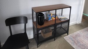 Une pièce comprenant une chaise noire, une console en bois sur laquelle repose un panier en treillis noir, et un tableau encadré accroché au mur.