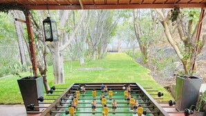 Uma mesa de futebol de mesa sob uma pérgola de madeira, com vista para um gramado e árvores.