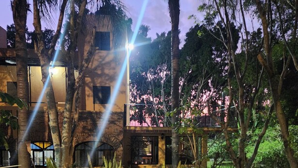 Um caminho leva a um edifício com varanda com vista para um jardim com árvores floridas.
