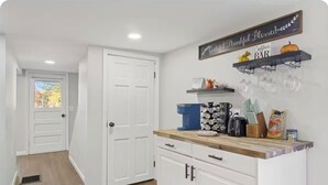 A kitchen with white cabinets, a wooden countertop, and a coffee bar area with a sign above.