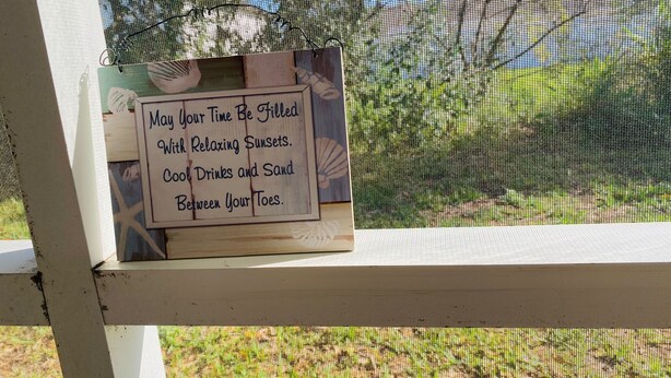 Un letrero de madera con un mensaje sobre relajarse con puestas de sol, bebidas refrescantes y arena entre los dedos.