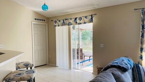 A room with a sliding glass door leading to an outdoor area, a sofa, a small table, and a ceiling light. - Near Beach-3br-sleeps6-patio-garden-parking-ac (Edgewater)
