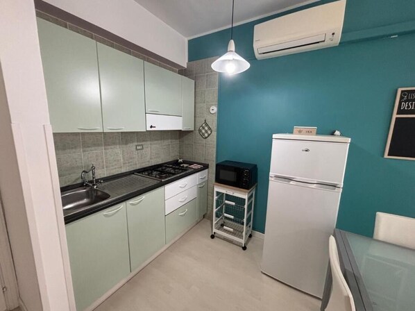 A compact kitchen with teal walls, a white refrigerator, a microwave, and a sink.