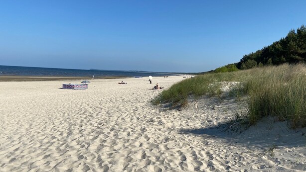 A sandy beach with a clear sky, a few people, and some beach umbrellas. - The yellow house at the harbor (Wolgast)